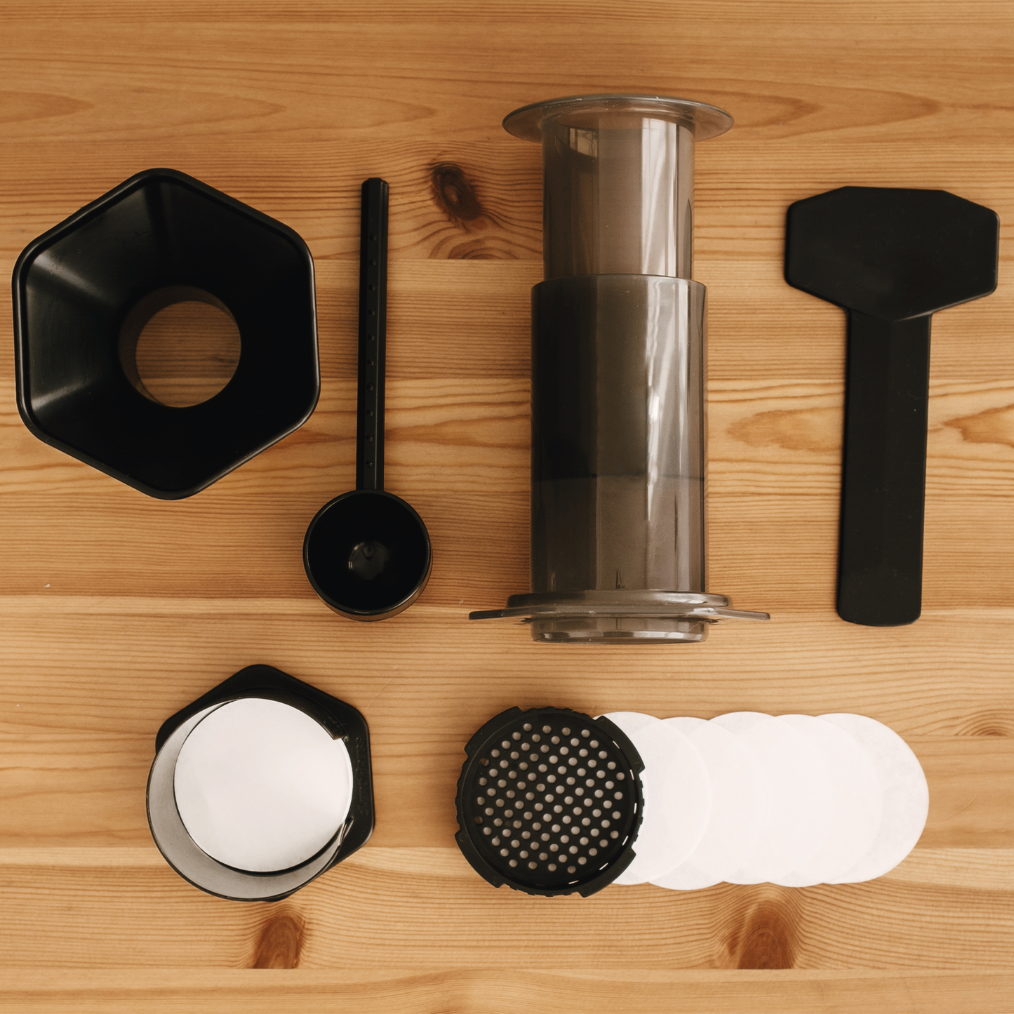 Filtros de AeroPress, AeroPress y sus accesorios presentados sobre madera
