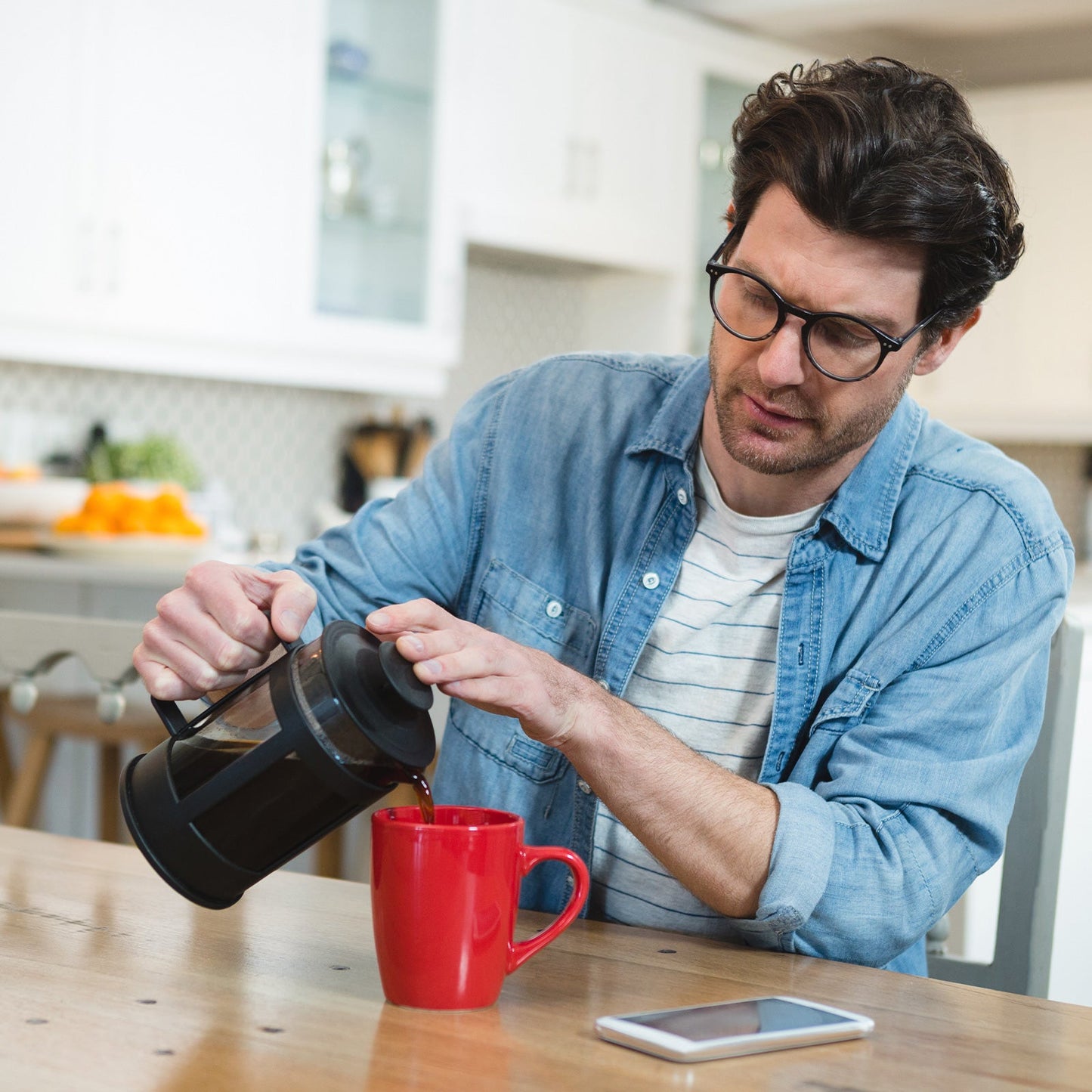 Joven virtiendo café desde una prensa francesa a una taza