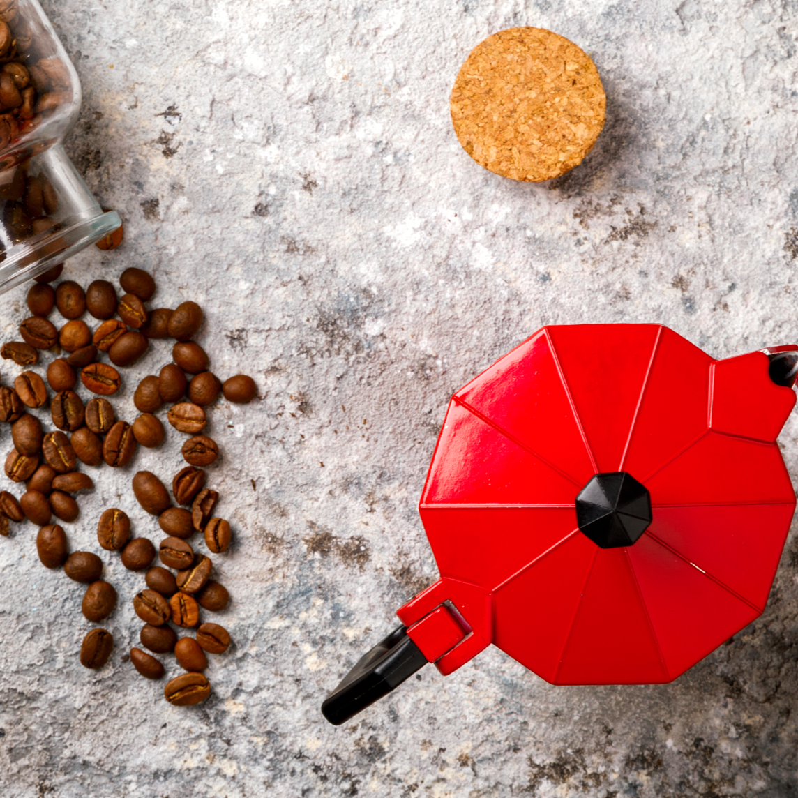 Cafetera italiana roja junto a granos de café vistos desde arriba