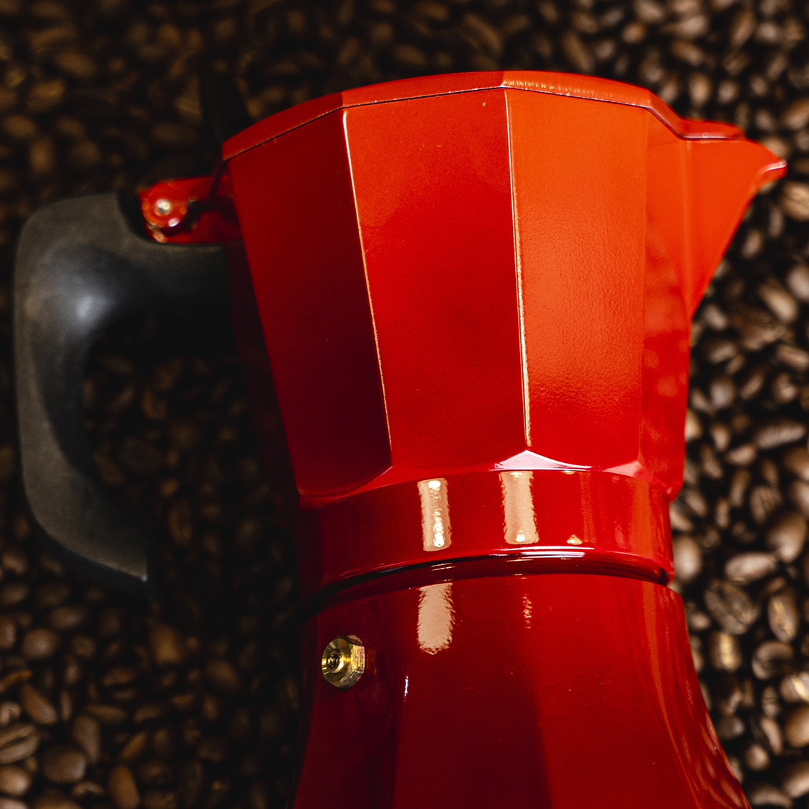 Cafetera italiana roja Oroley acostada sobre un manto de café Tarco