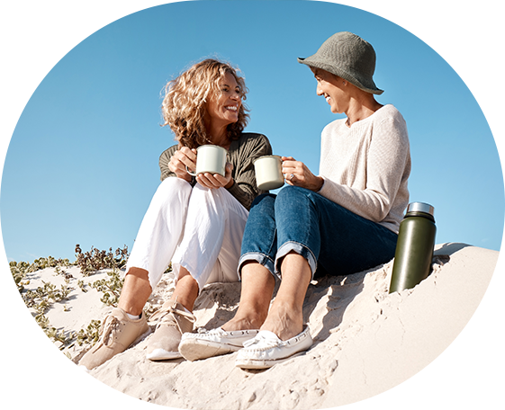 Dos mujeres sentadas en una duna tomando café en tazas