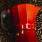 Cafetera italiana roja Oroley acostada sobre un manto de café Tarco